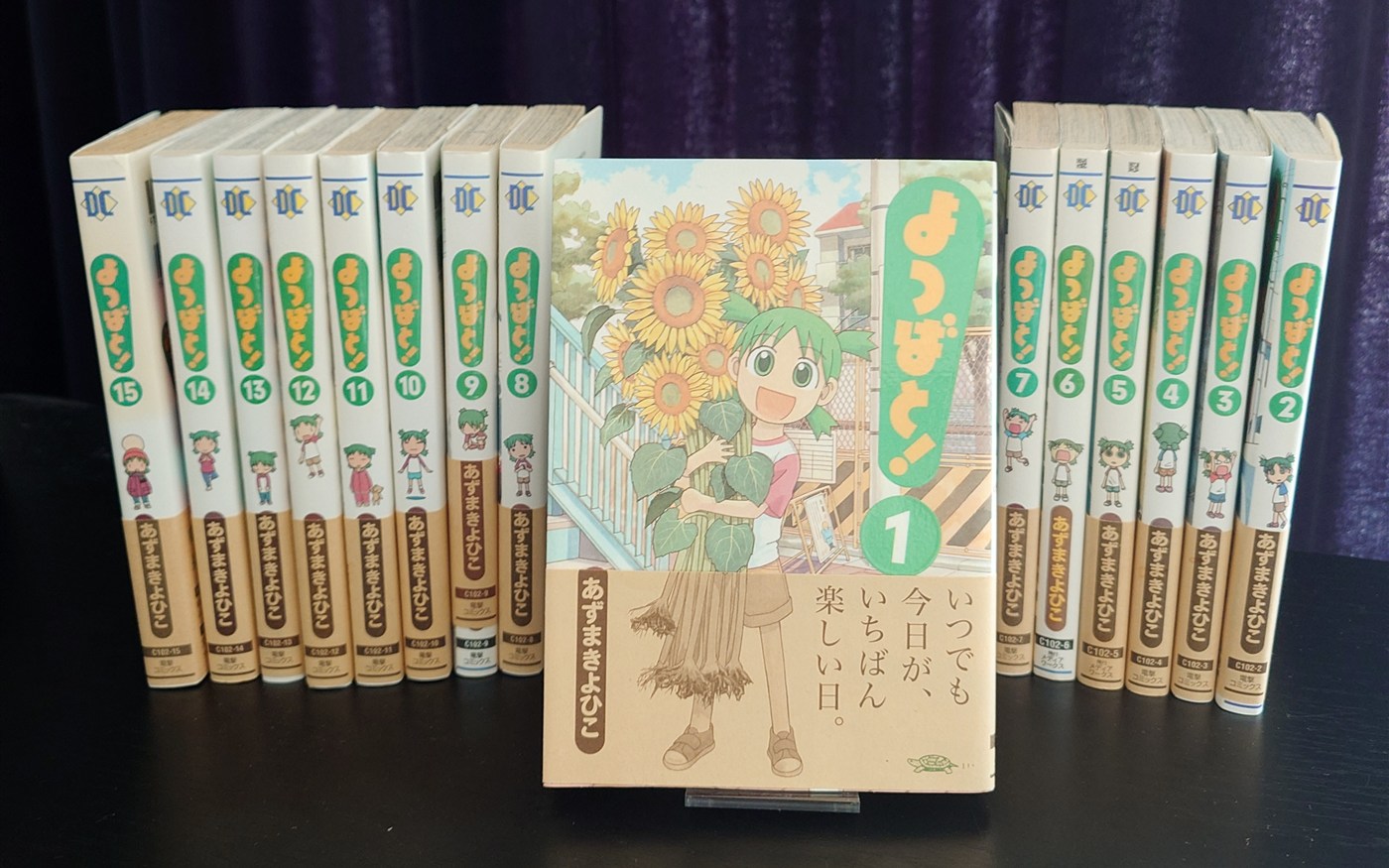 Japanese Yotsuba&! volumes lined up on a shelf, with Volume 1's sunflower cover displayed in front.